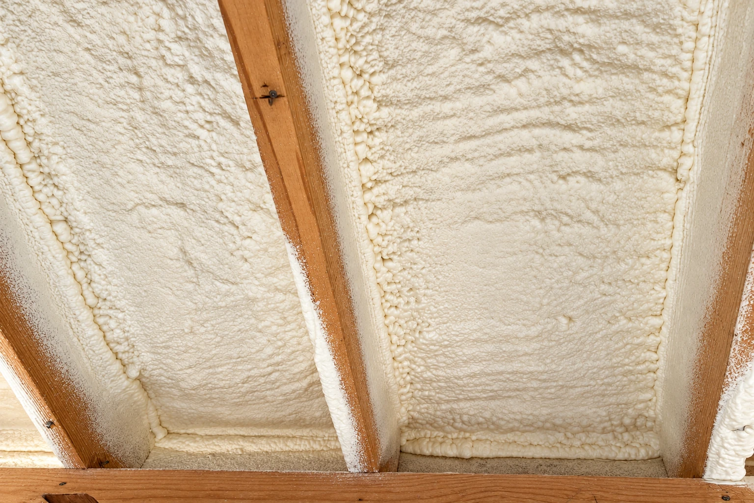 Close view of white closed-cell spray foam filling the spaces between wooden rafters.